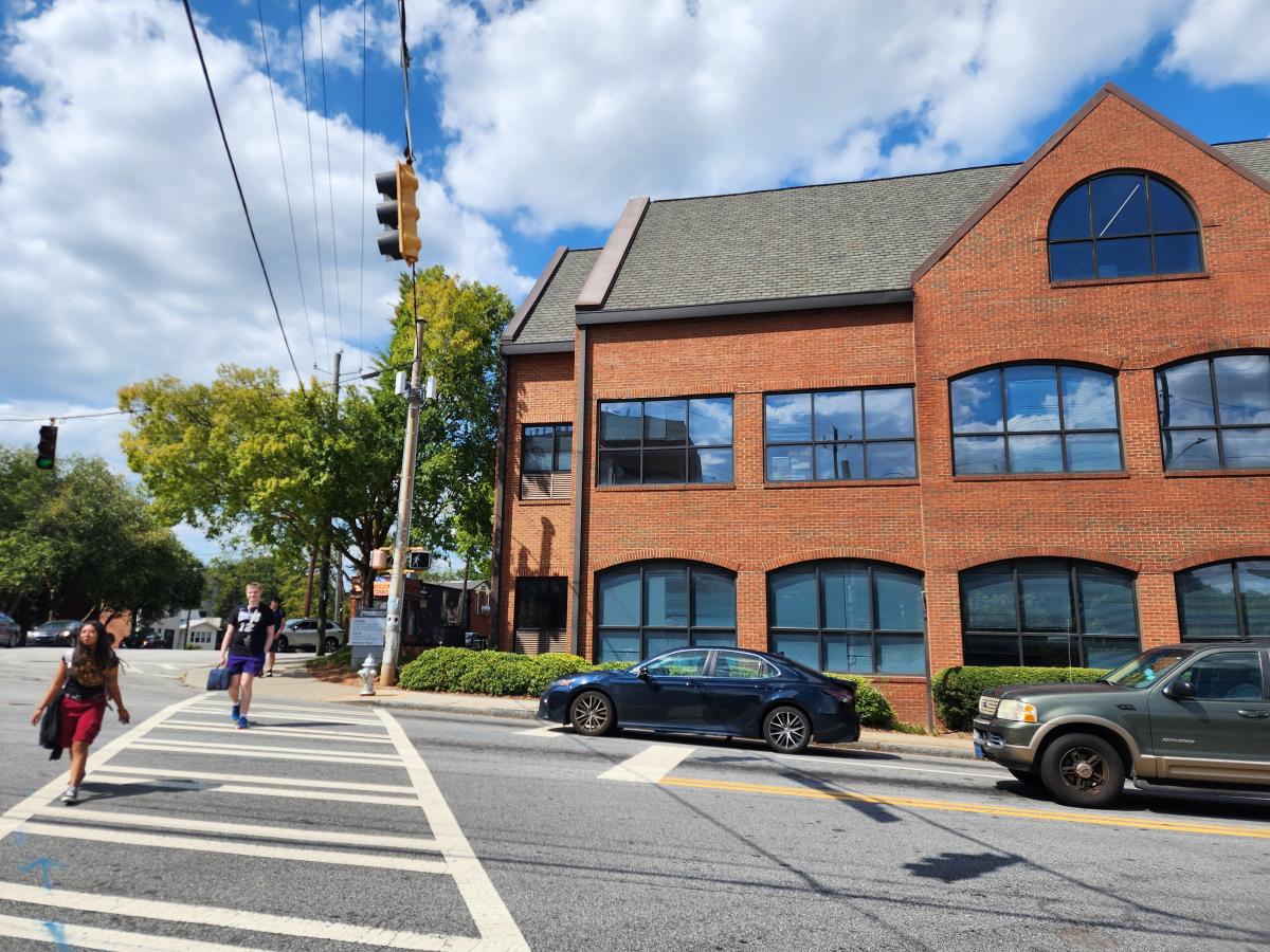 People crossing a busy street. Brick three-story building in the background.